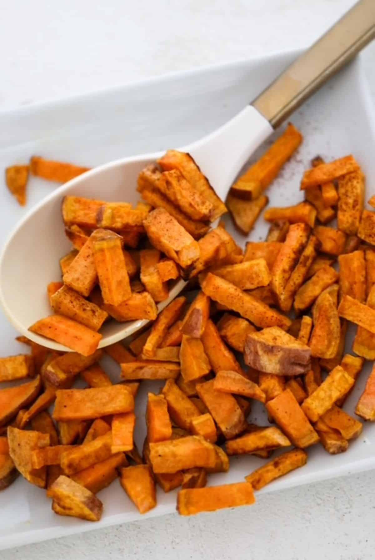 Air fryer roasted sweet potato chunks on a white serving plate with a white and gold serving spoon.