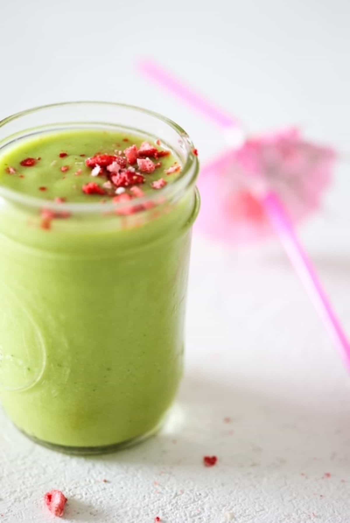 One green smoothie in a mason jar with a pink tropical straw to the side.