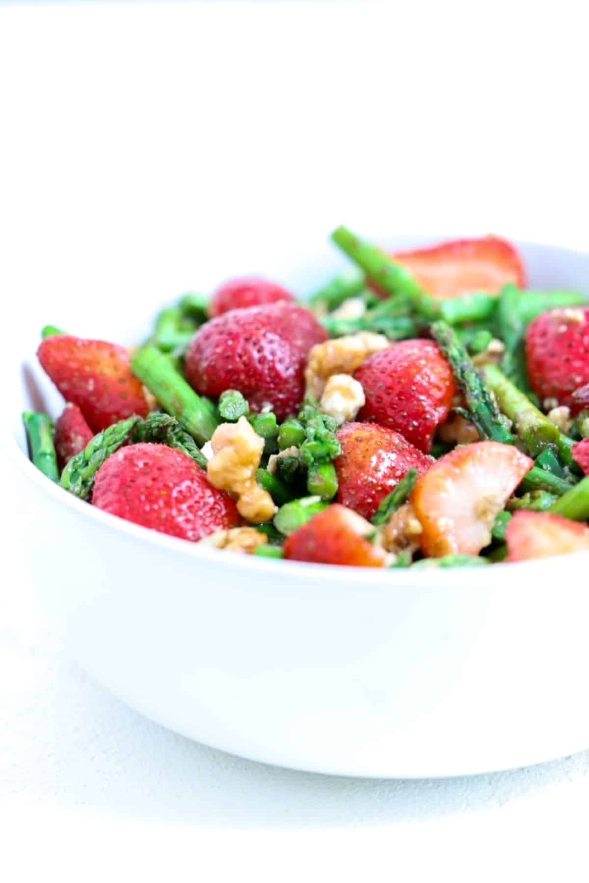 Cold asparagus salad with strawberries in a white serving bowl.