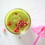 Top view of a green smoothie in a glass mason jar topped with crushed dried strawberry pieces.