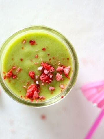 Top view of a green smoothie in a glass mason jar topped with crushed dried strawberry pieces.
