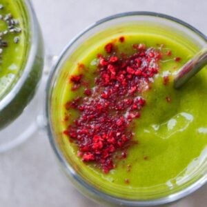 Up-close image of green island smoothie in a glass mug topped with crushed freeze-dried strawberries and served with a stainless-steel straw.