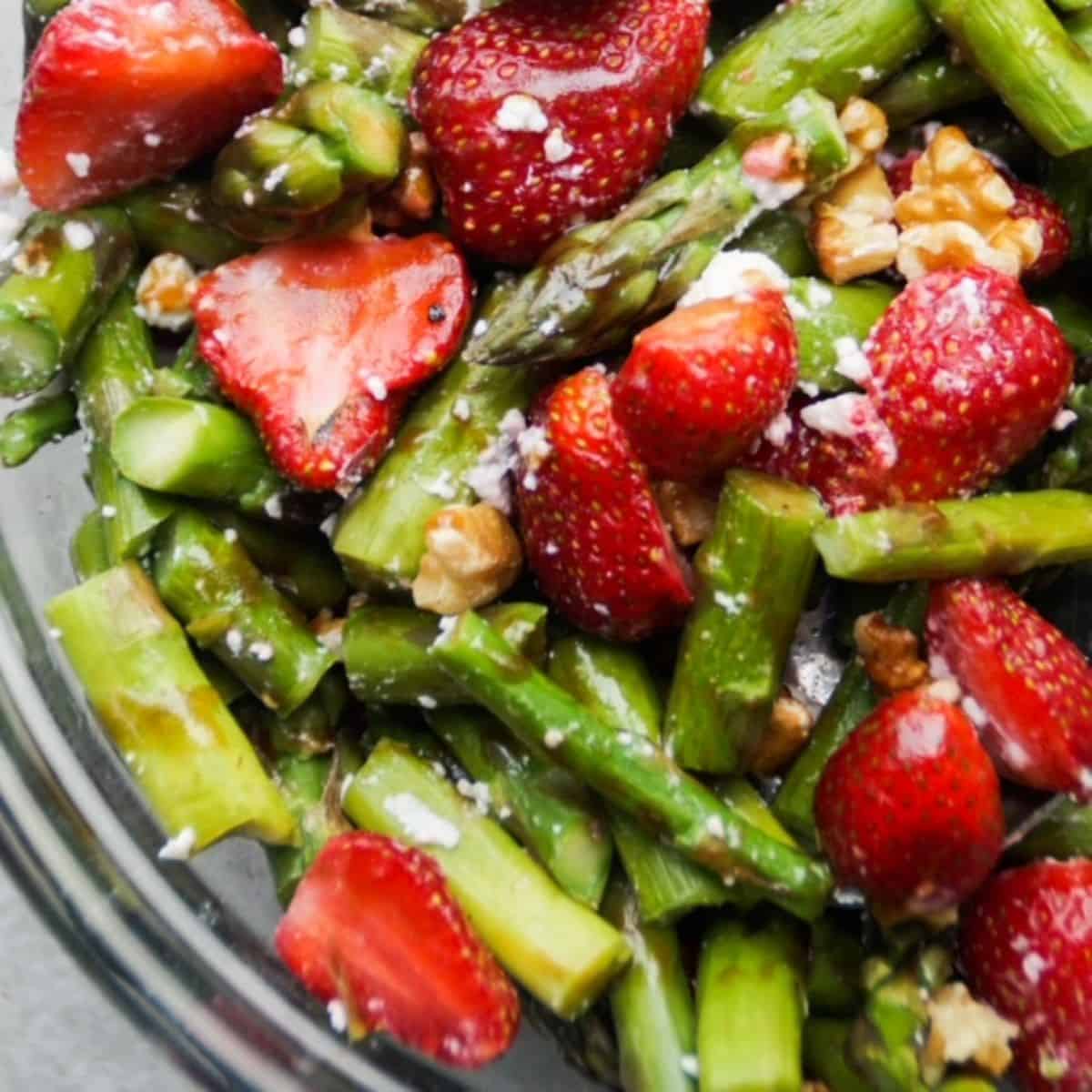 Cold asparagus salad with strawberries in a glass bowl.