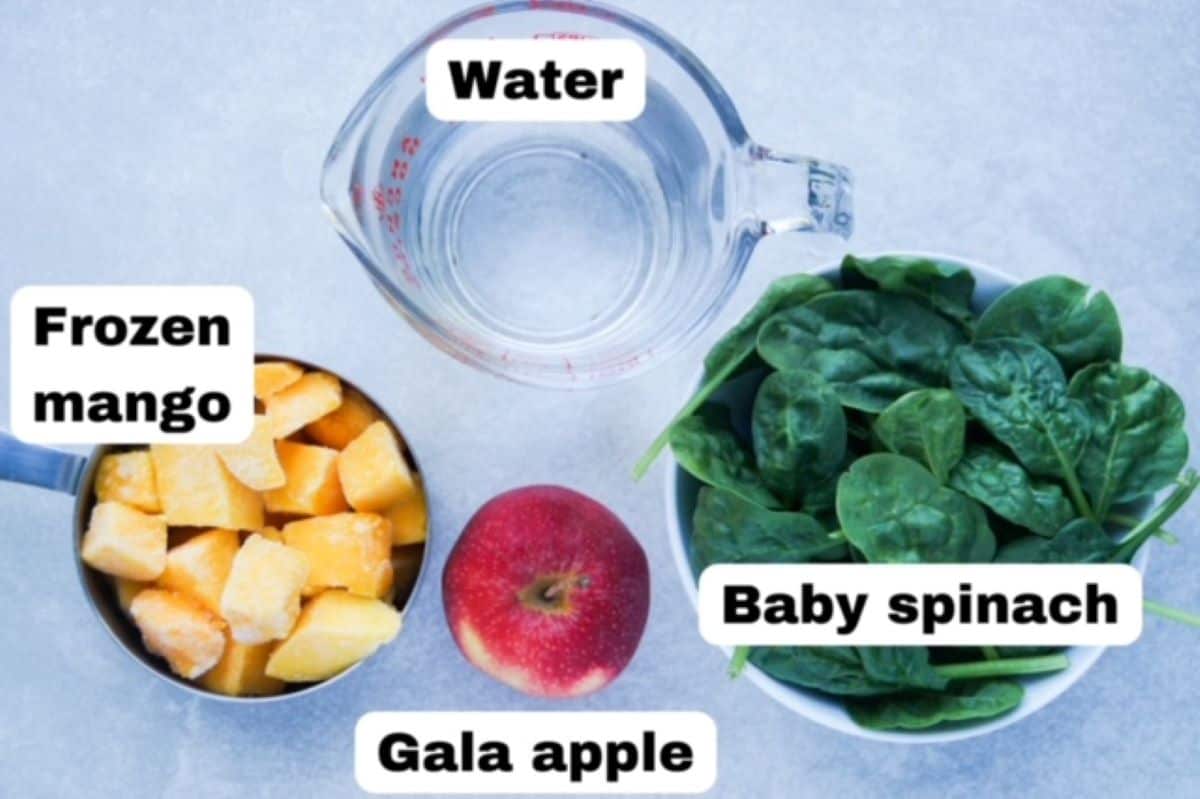 Frozen mango and water in separate measuring cups, one gala apple, one bowl of baby spinach. All ingredients are labeled.