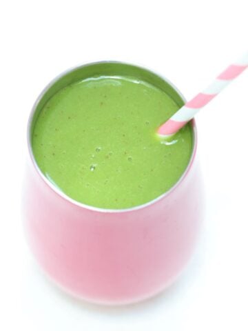 Spinach mango smoothie in a pink tumbler with a pink and white striped straw.