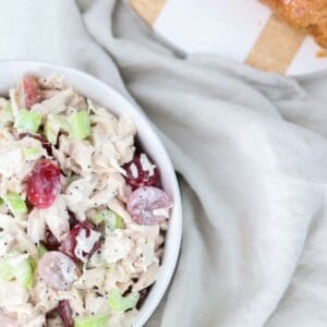 Chicken salad in a white bowl with a linen napkin and serving board to the side.