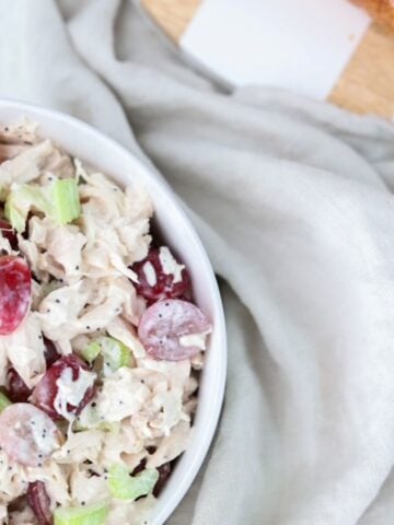 Chicken salad in a white bowl with a linen napkin and serving board to the side.
