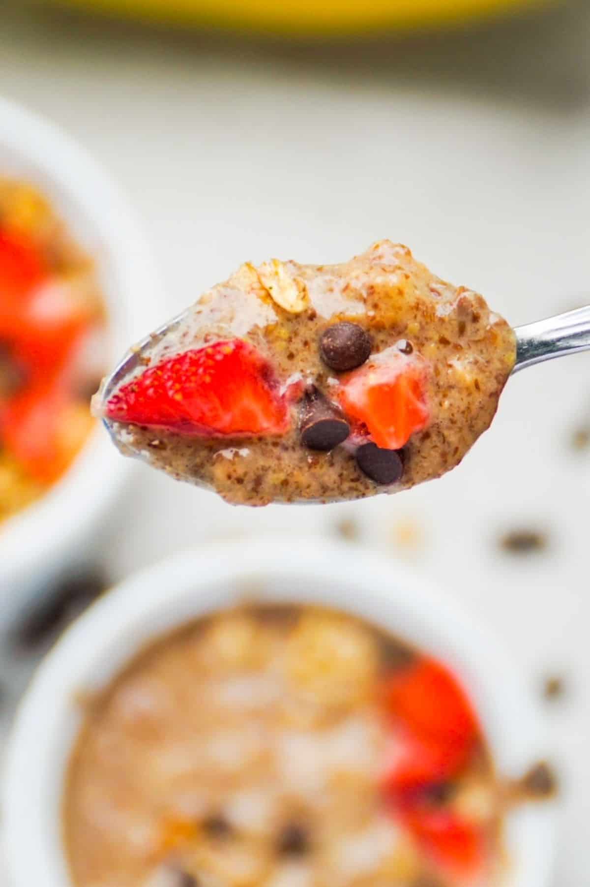 One spoonful of flaxseed pudding topped with strawberry pieces and mini chocolate chips up close with two small bowls of flaxseed pudding in the background.