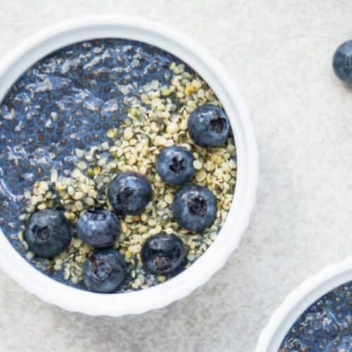 Blue chia pudding topped with hemp hearts and fresh blueberries in a small white round bowl.