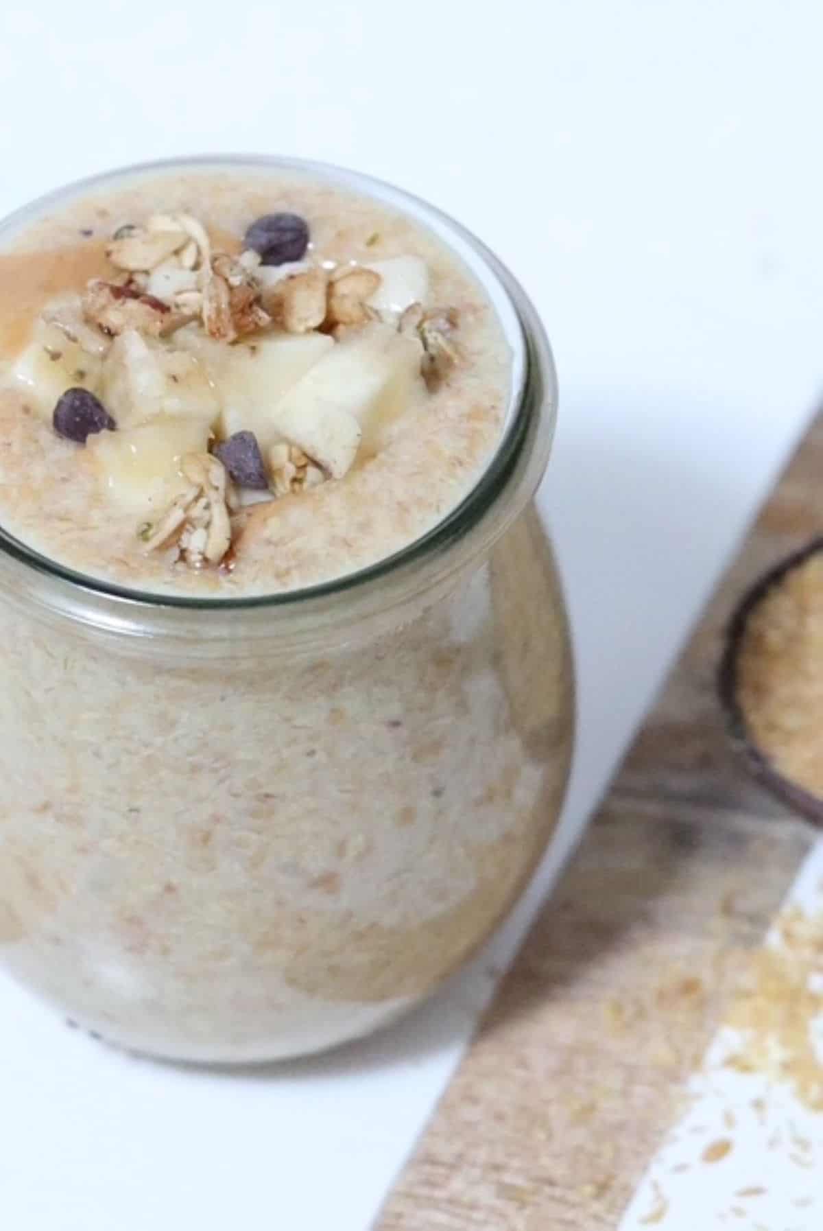 Peanut Butter Flaxseed Pudding in a tulip shaped glass jar topped with fresh banana, granola, and mini chocolate chips.