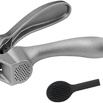 One garlic press laying on its side with the small scraper it comes with next to it.