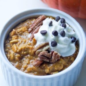 Top view of pumpkin overnight oats in a small white ramekin topped with pecans, whipped cream, and mini chocolate chips.