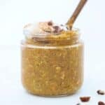 Pumpkin Spice Overnight Oats topped with whipped cream and chopped pecans in a jar with a small wooden spoon.