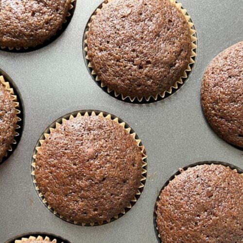 Two whole and five partial chocolate cupcakes in a lined muffin tin.