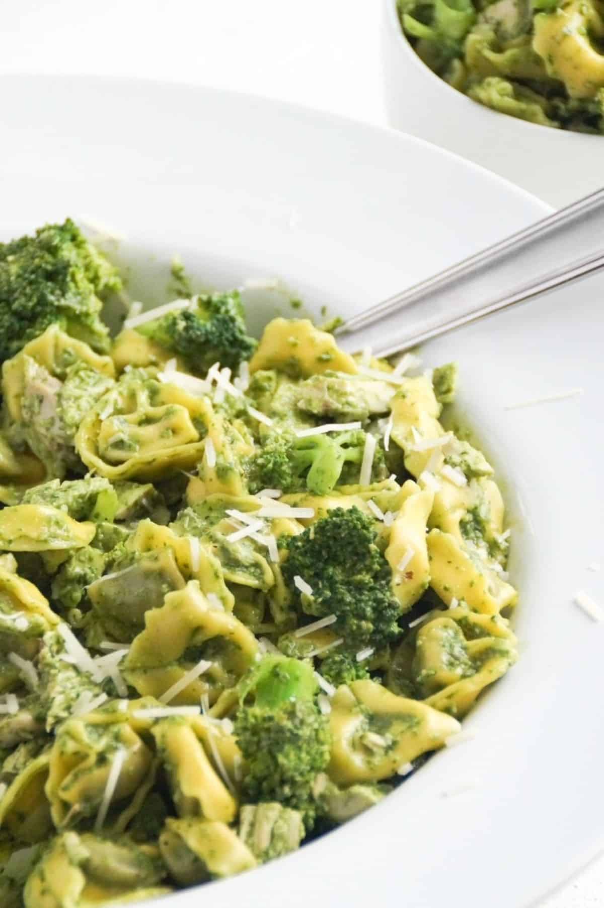 Pesto with tortellini, chicken, and broccoli in a large white serving bowl with a spoon.