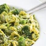 Pesto with tortellini, chicken, and broccoli in a large white serving bowl with a spoon.