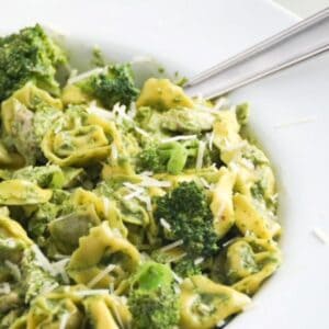 Pesto with tortellini, chicken, and broccoli in a large white serving bowl with a spoon.
