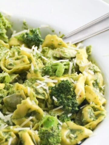 Pesto with tortellini, chicken, and broccoli in a large white serving bowl with a spoon.