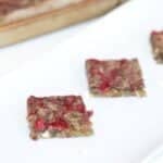 Two Raspberry and White Chocolate Blondies on a white platter with a bar pan of blondies in the background.