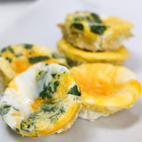 Baked eggs in a muffin tin, some are plain egg, and some have spinach and cheese.