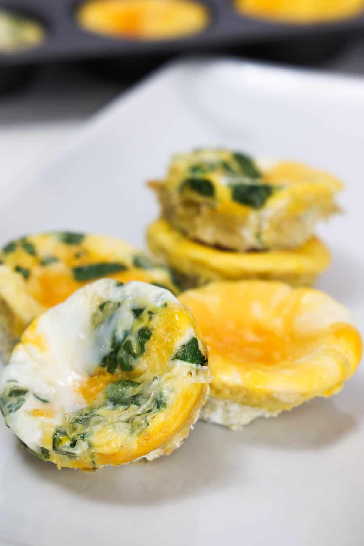 Baked egg muffins, some plain and some with spinach, on a white plate.