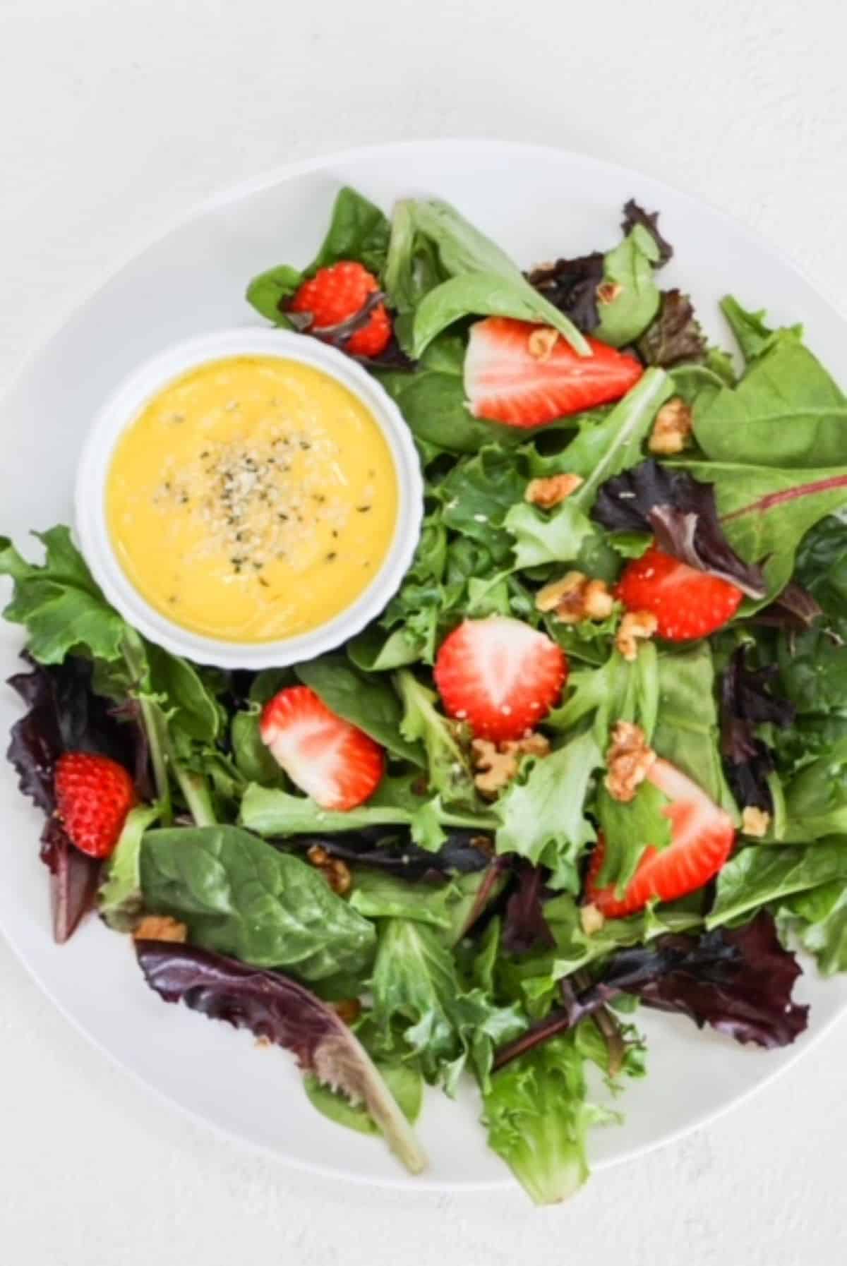 Mango salad dressing plated with a strawberry salad on a white plate.