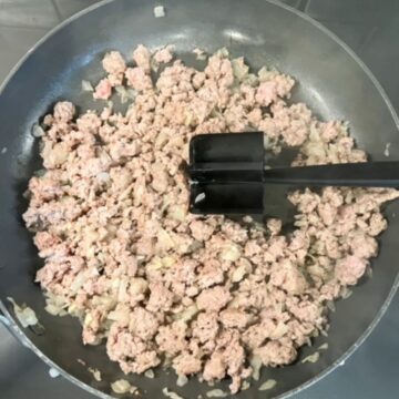 Cooked ground turkey in a skillet with a food masher.