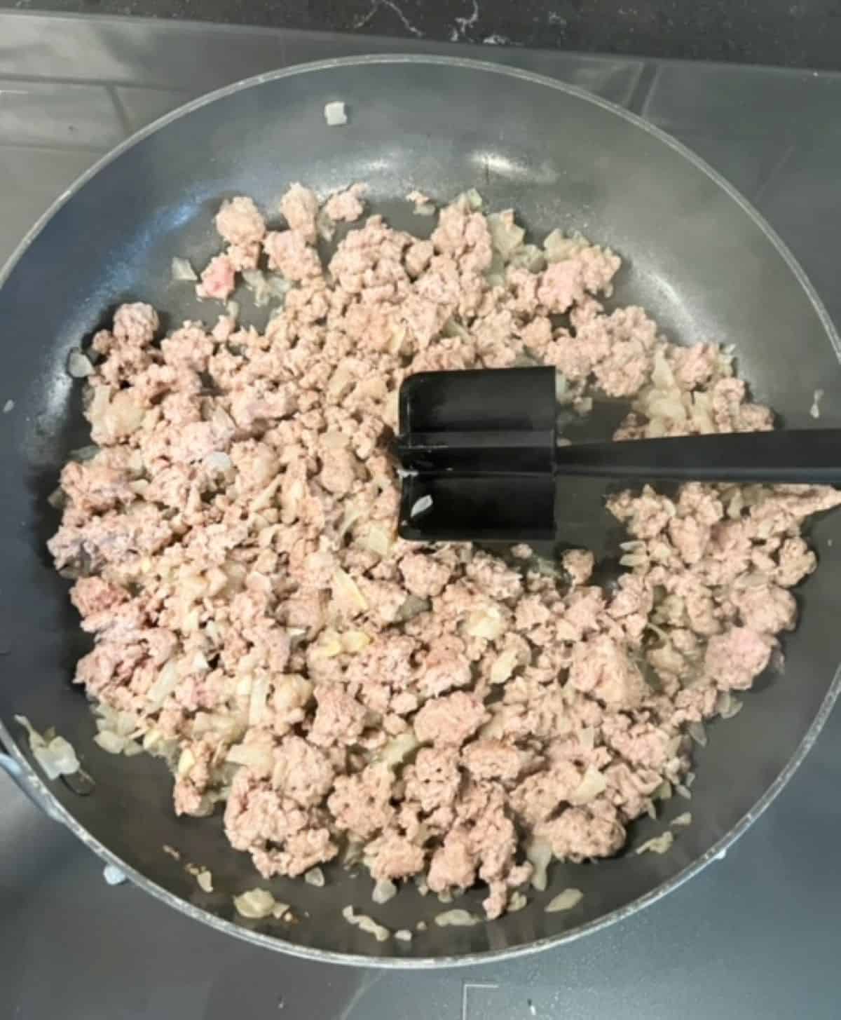Cooked ground turkey in a skillet with a food masher.