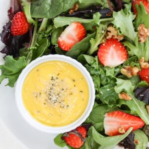 Mango salad dressing topped with hemp hearts alongside a strawberry salad on a white plate.