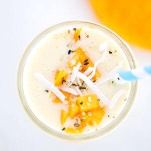Creamy Mango Pineapple Smoothie topped with mango and coconut flakes with a blue and white striped straw.