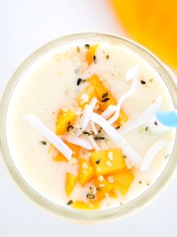 Creamy Mango Pineapple Smoothie topped with mango and coconut flakes with a blue and white striped straw.