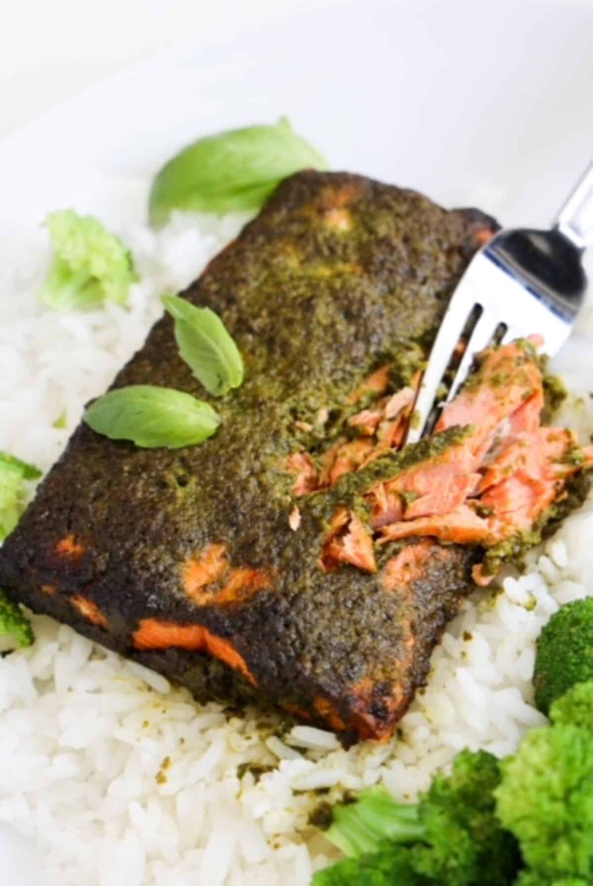 A fork cutting into a piece of cooked salmon topped with pesto.