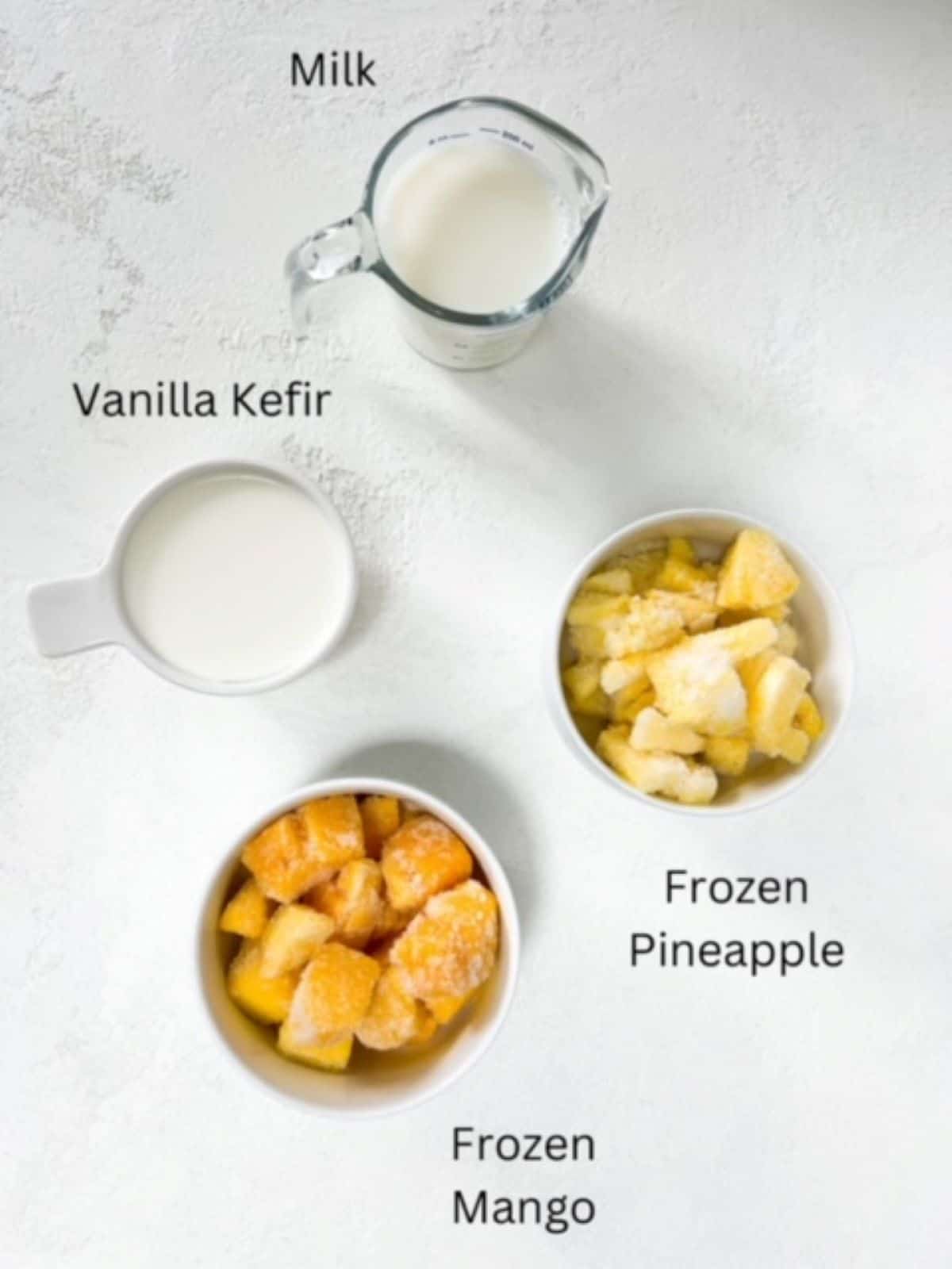 Milk, kefir, frozen pineapple, and frozen mango in individual serving-ware, labeled.