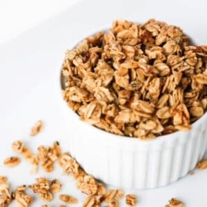 Granola in a white ramekin with pieces of granola scattered around the base of the ramekin.