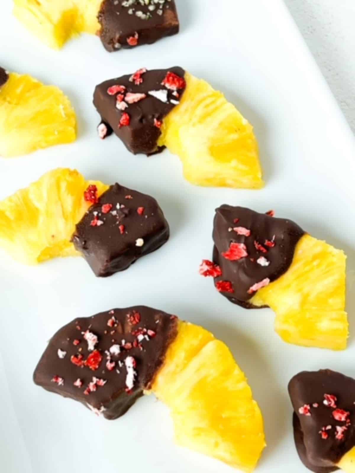 Thirds and halves of pineapple rings with one end covered in chocolate and topped with crushed freeze dried strawberries.