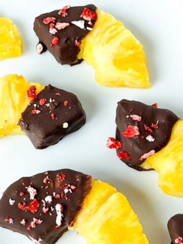 Thirds and halves of pineapple rings with one end covered in chocolate and topped with crushed freeze dried strawberries.