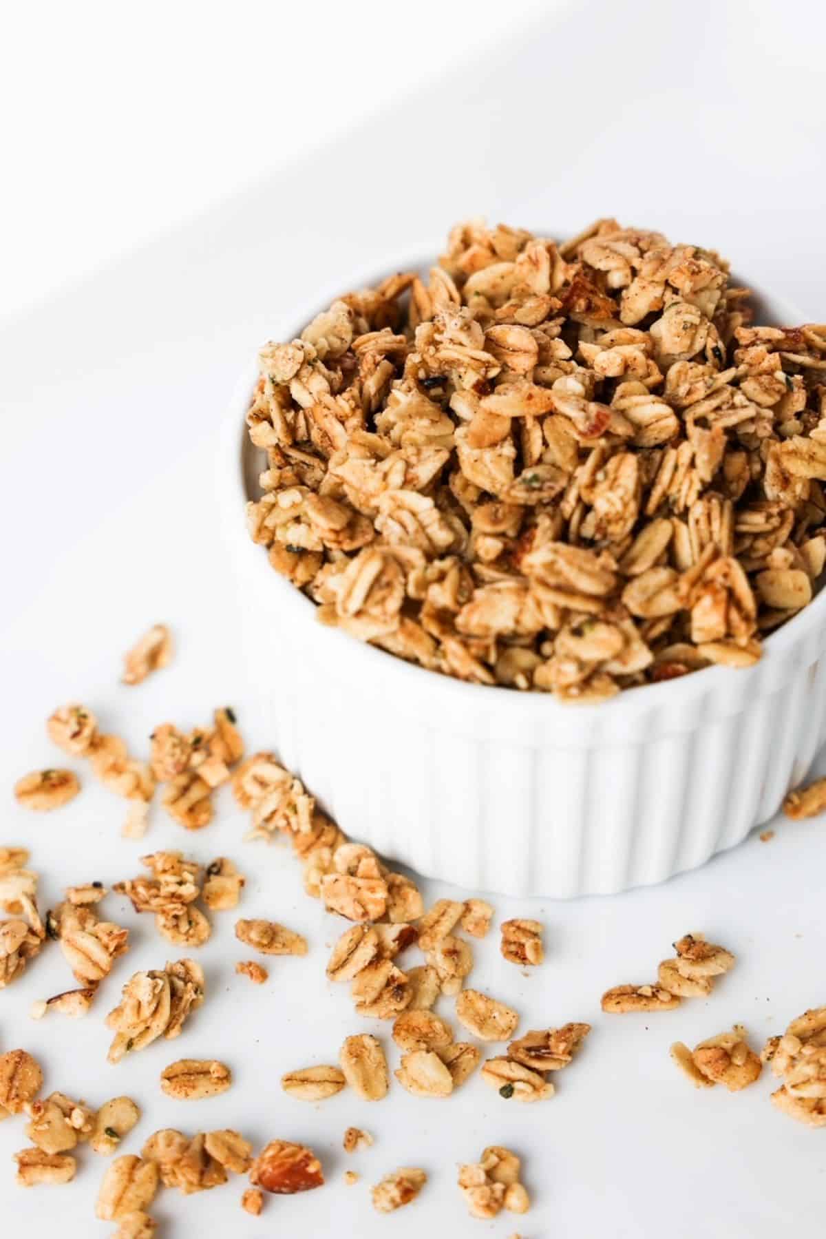 Granola in a white ramekin with pieces of granola scattered around the ramekin.