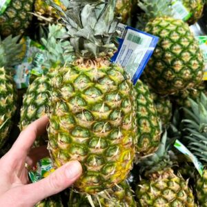 One ripe pineapple with a still on held up over a pile of pineapples.