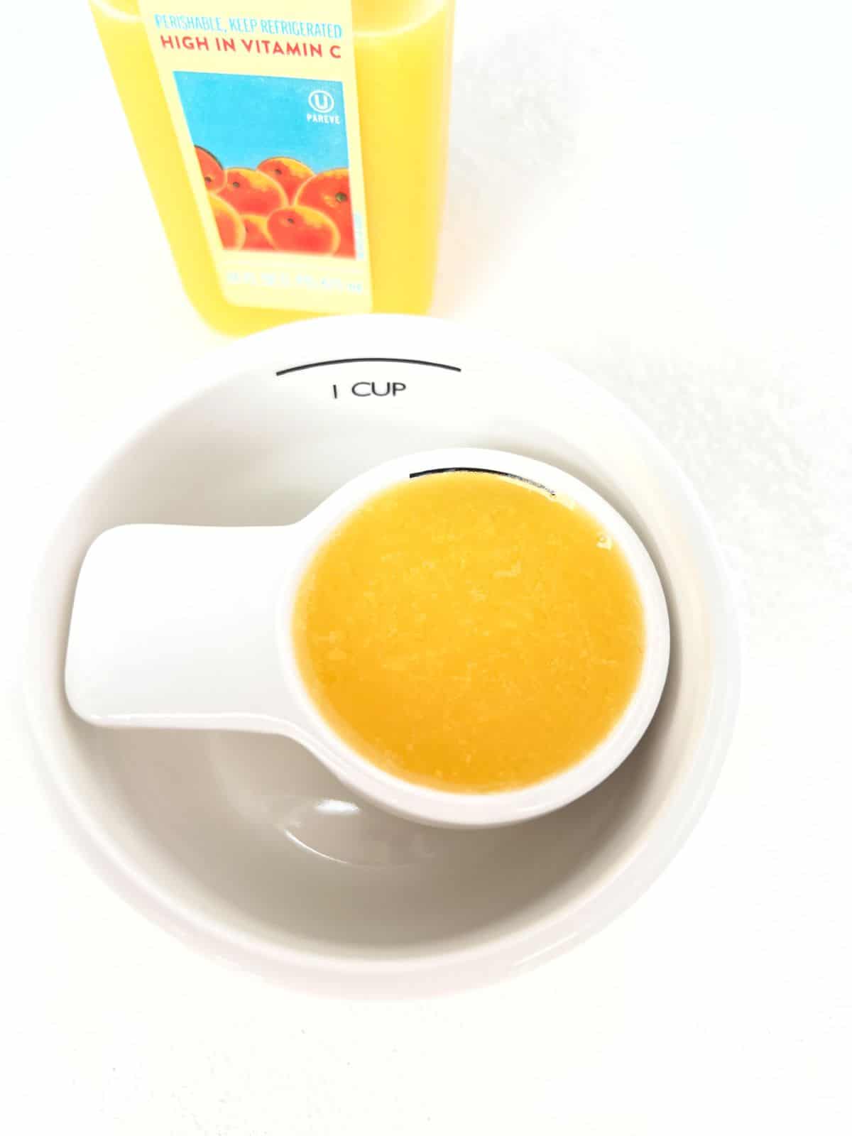 A quarter cup measuring cup filled with orange juice inside of a one cup measuring cup.