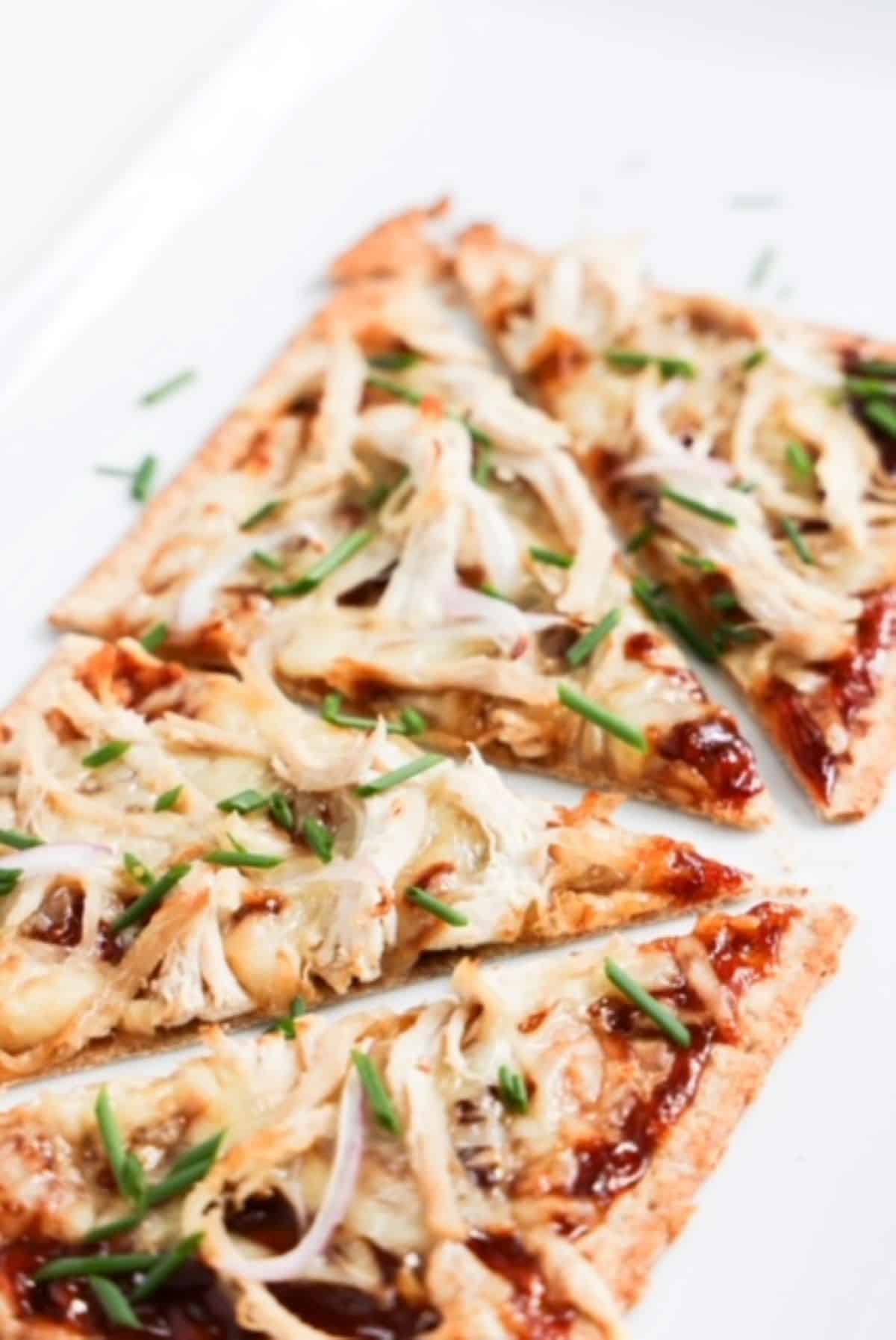 One bbq chicken flatbread topped with chopped green onion and sliced into four pieces.