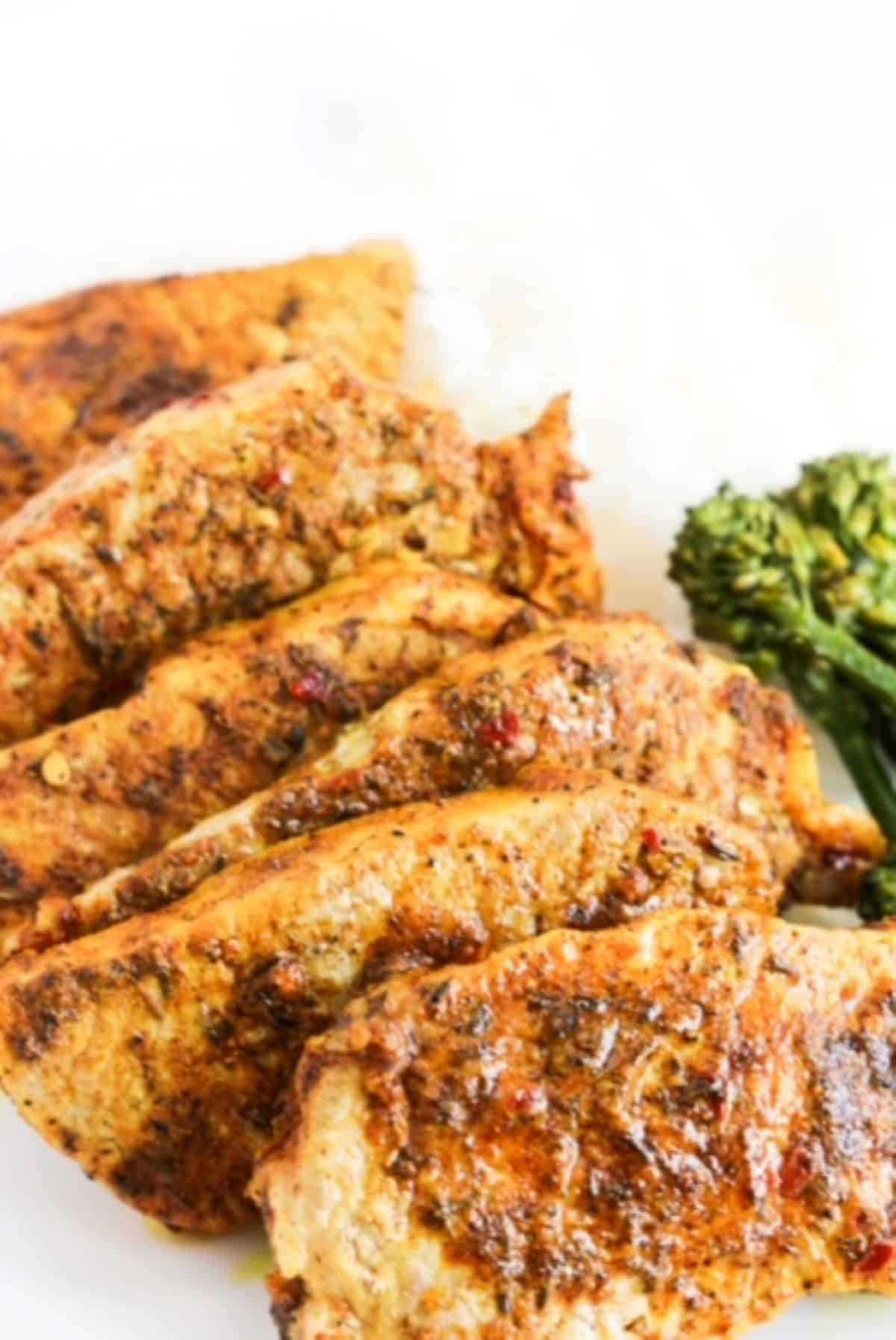 Six cooked jerk lime marinated pork chops overlapping each other on a white plate with broccolini to the right.