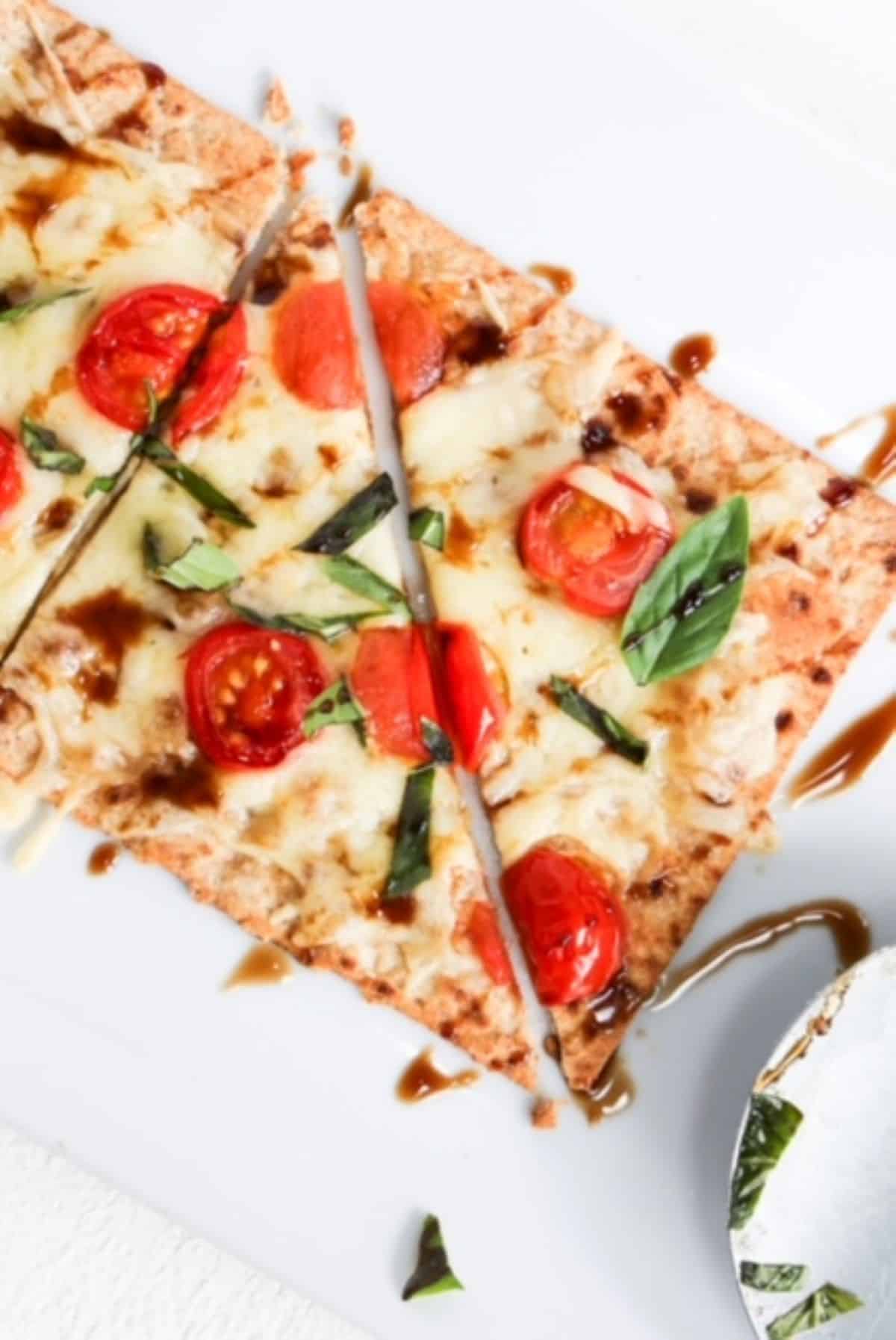 Margherita flatbread on a white plate with a pizza roller to the right.