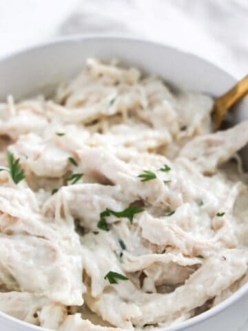 Chicken in white sauce served in a white bowl with a golden spoon.