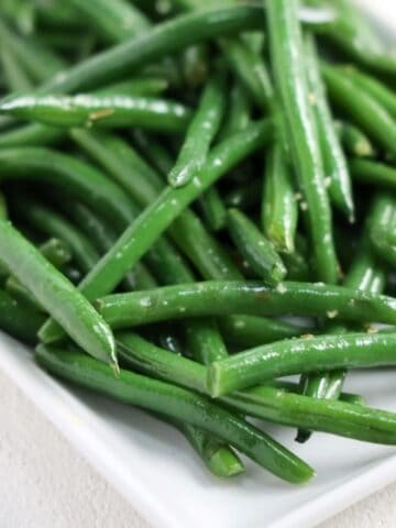 Sauteed garlicky green beans on a white rectangle shaped dish.