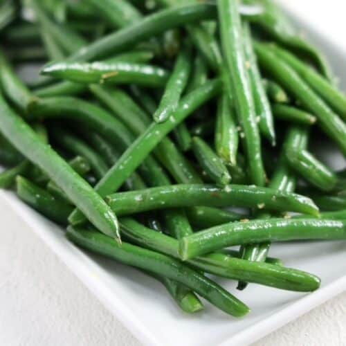 Sauteed garlicky green beans on a white rectangle shaped dish.