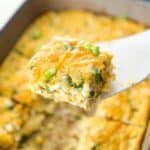 One piece of egg casserole held up by a white spatula over the rest of the casserole.