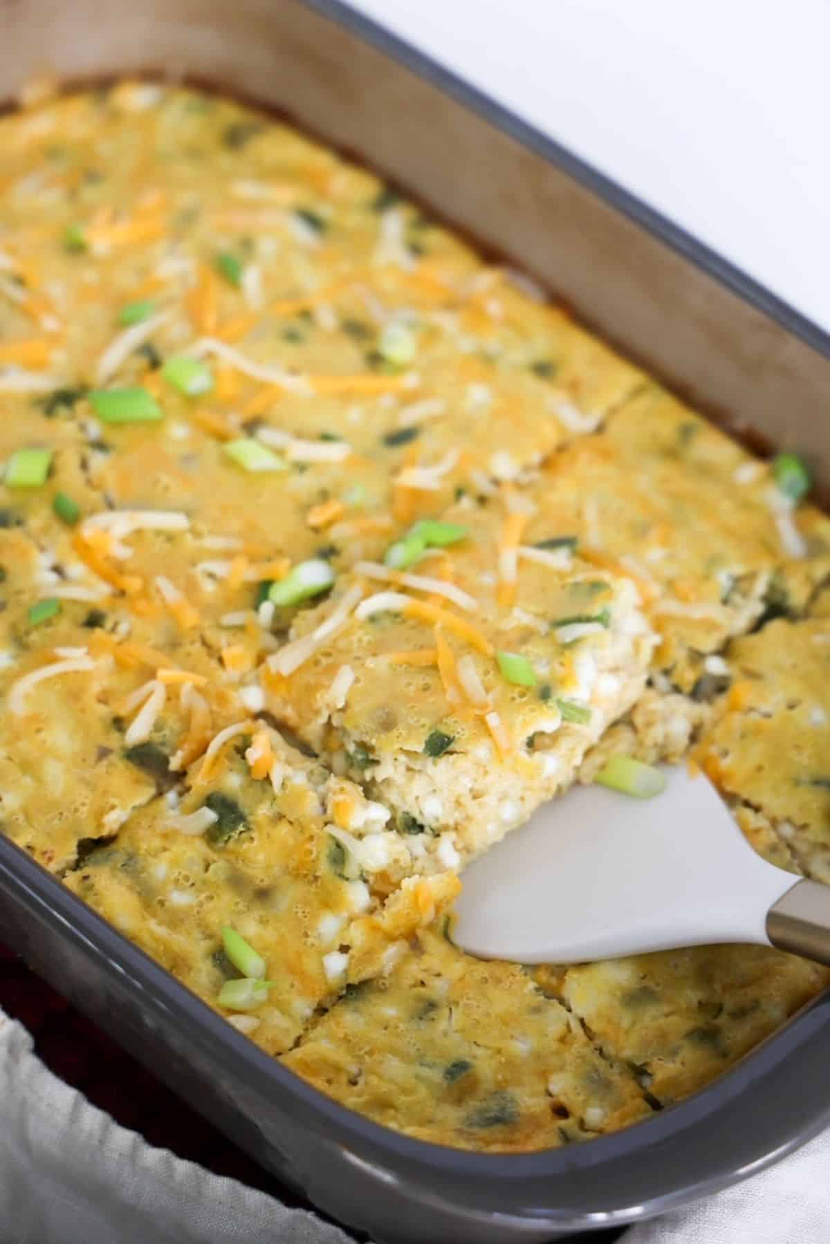 Green chile egg casserole in a large baking dish with one piece being removed with a white and gold spatula.