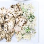Pieces of Italian chicken with orzo and broccoli to the side.