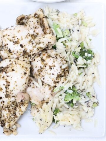 Pieces of Italian chicken with orzo and broccoli to the side.