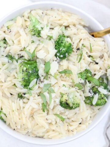 Top view of orzo with broccoli in a white serving dish with a gold serving spoon.